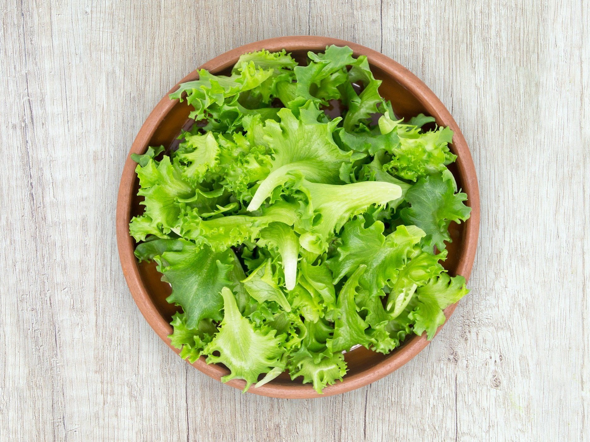 unsplash-image-PcJi7LH_1dQ (1) Fresh green lettuce leaves in a brown ceramic bowl on a wooden surface, ideal for salads and healthy meals.
