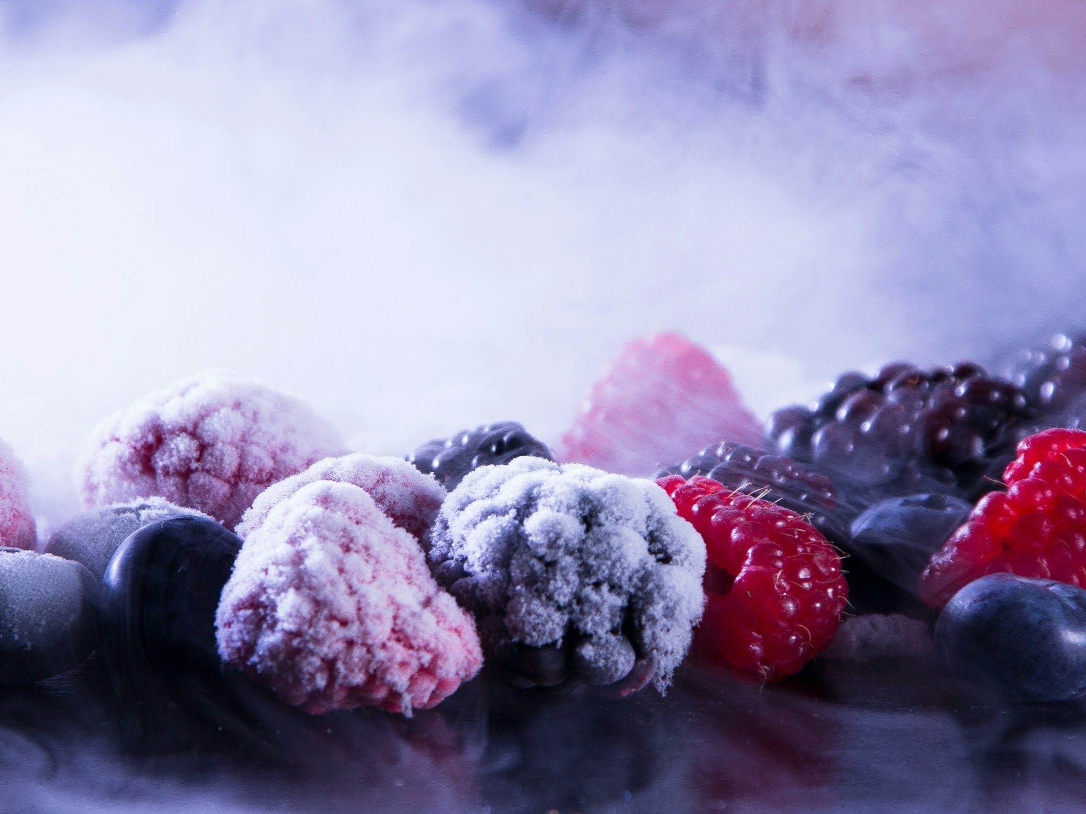unsplash-image-X5ChCOu8CQg Frozen berries including raspberries, blackberries, and blueberries, covered in frost, arranged on a reflective surface with a misty background. Ideal for healthy recipes or smoothie ideas.